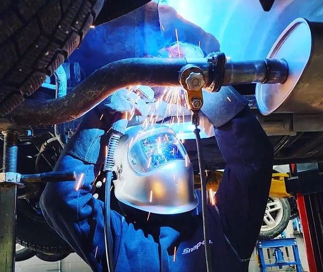Technician welding an exhaust section under a vehicle on the hoist at Level Auto